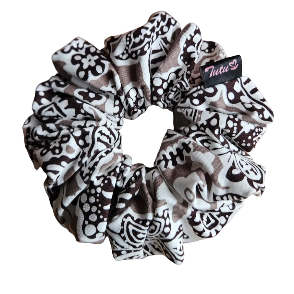 A fabric hair scrunchie with a black, white, and taupe floral pattern, resting on a white background. A small black brand tag with pink script reading 'Tutu22' is visible on the side.