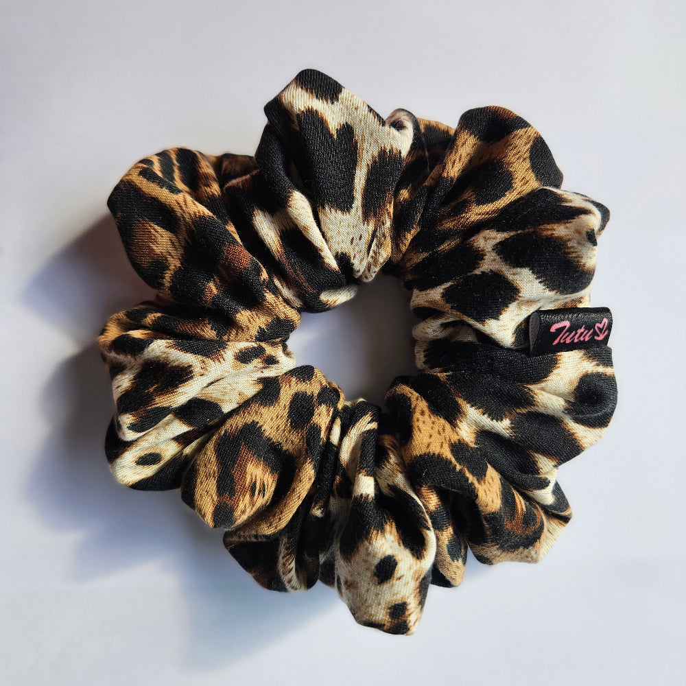 A leopard print fabric scrunchie with black, brown, and beige spots, featuring a small black brand tag that reads 'Tutu22'.