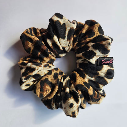 A leopard print fabric scrunchie with black, brown, and beige spots, featuring a small black brand tag that reads 'Tutu22'.