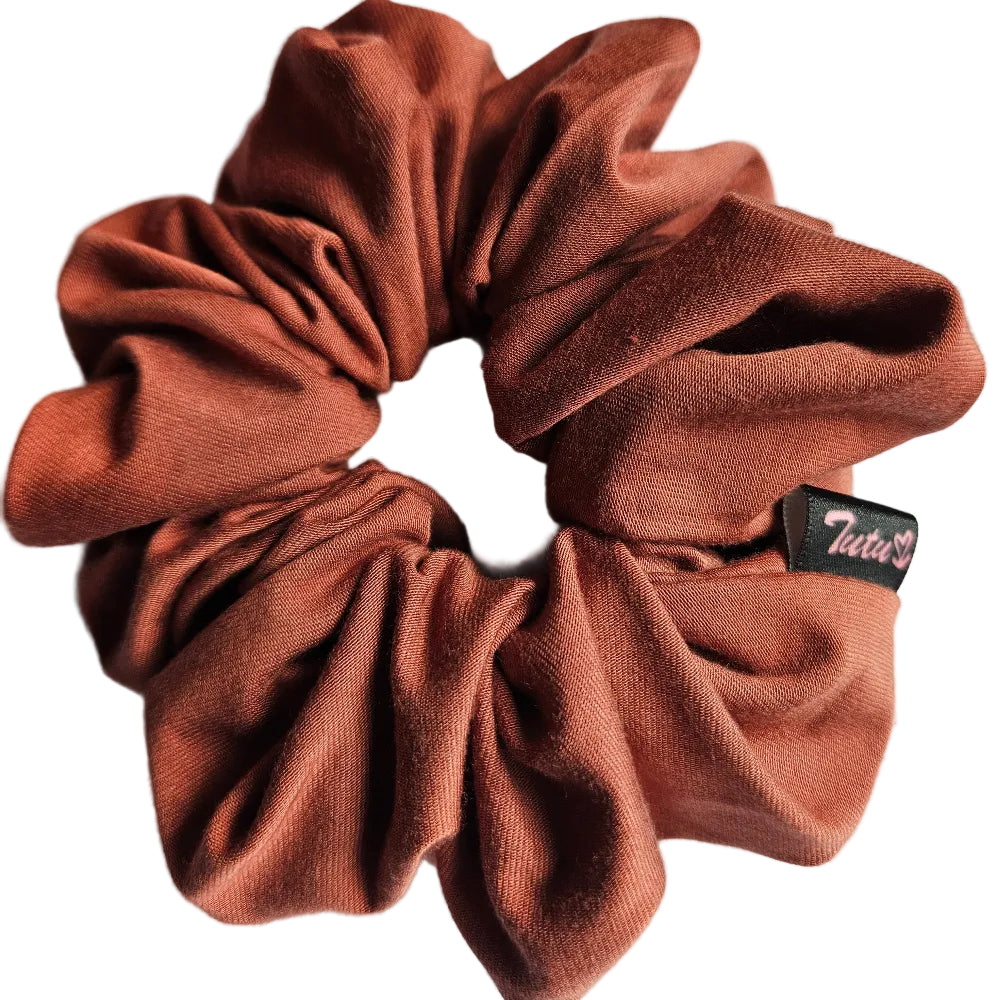 A burnt orange fabric scrunchie with a small black brand tag reading 'Tutuy22' on the side, photographed on a plain light background.