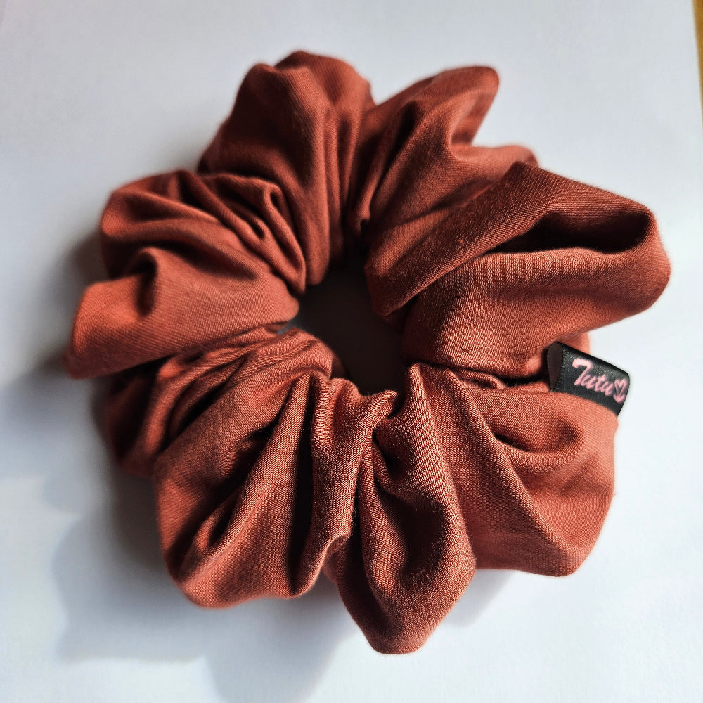 A burnt orange / terracotta stretch fabric scrunchie with a small black brand tag that reads 'Tutu22', photographed on a plain white surface.
