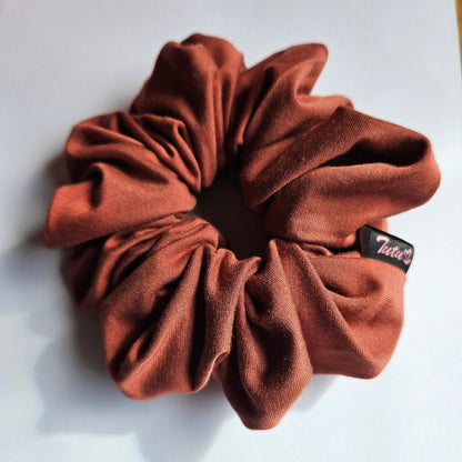 A burnt orange / terracotta stretch fabric scrunchie with a small black brand tag that reads 'Tutu22', photographed on a plain white surface.