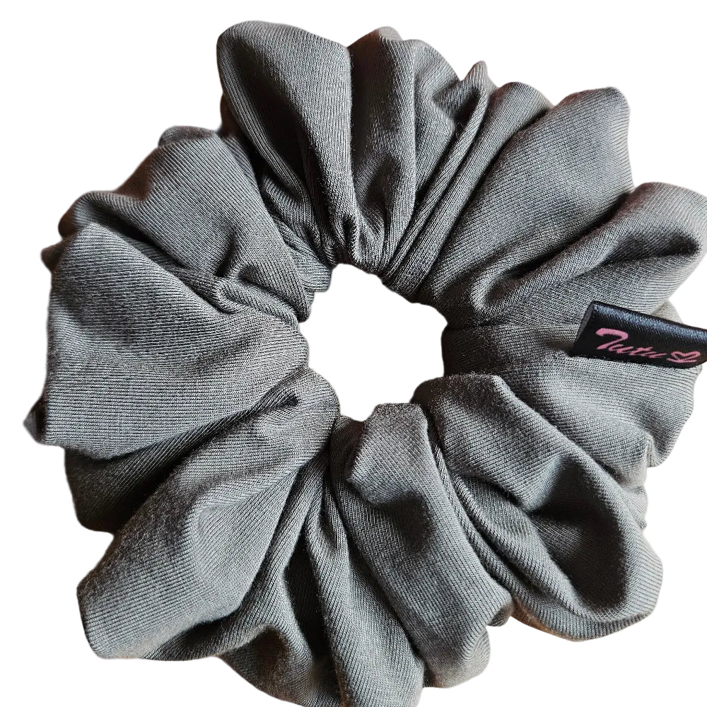 A olive green fabric scrunchie with a small black brand tag, resting on a light brown wooden surface.