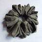 An olive green fabric scrunchie with a small black brand tag that reads 'Tutu22', photographed on a plain white surface.