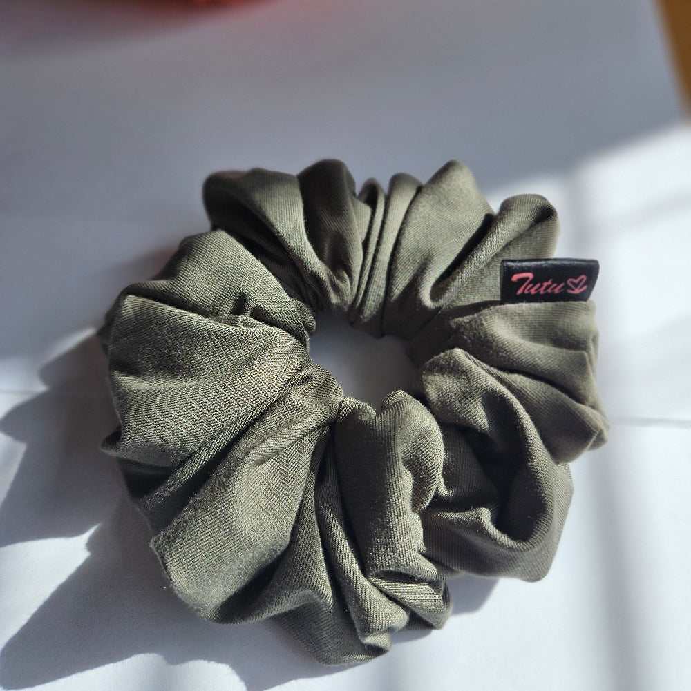 An olive green fabric scrunchie with a small black brand tag reading 'Tutu22', resting on a white surface with soft shadows.